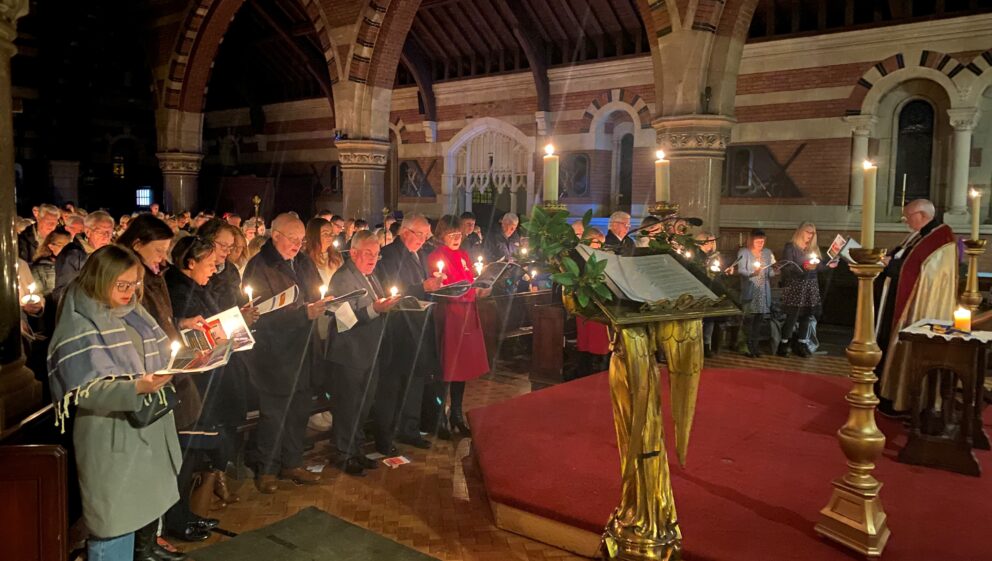 People holding candles and hymn sheets singing in a church