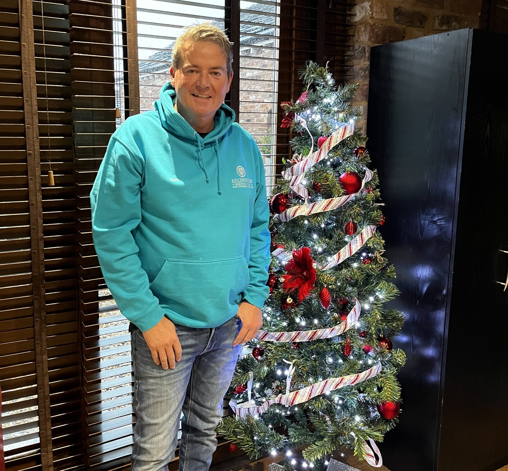 Man in a green hoodie stood in front of a Christmas tree