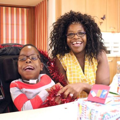 Mother with a disabled child sat smiling in a wheelchair with Christmas presents