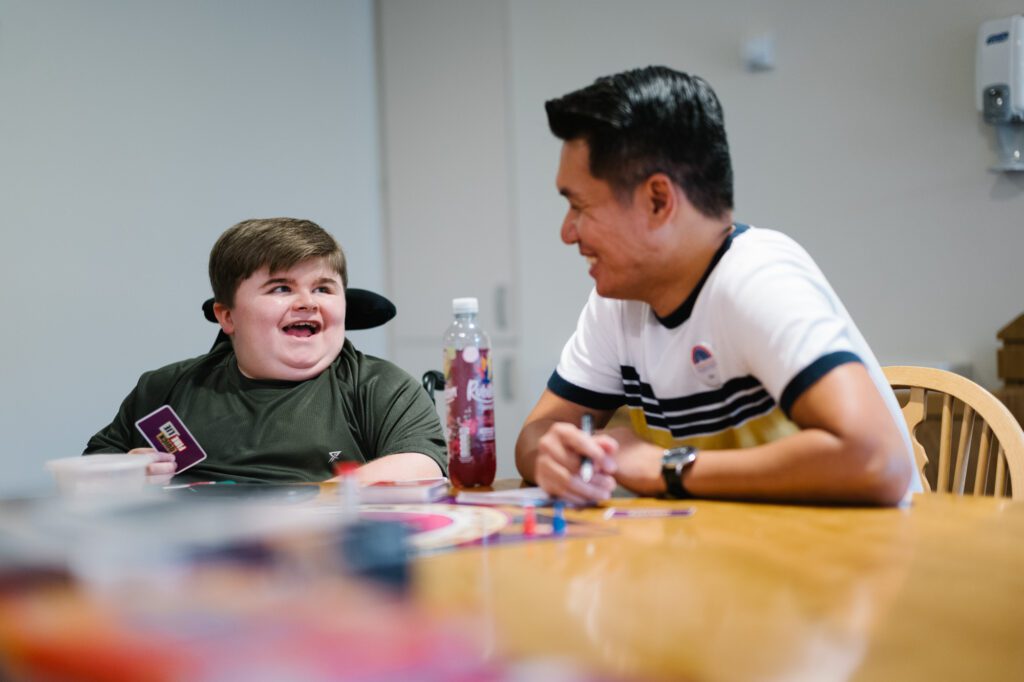 Two people seated at a table playing a card game smiling at each other 