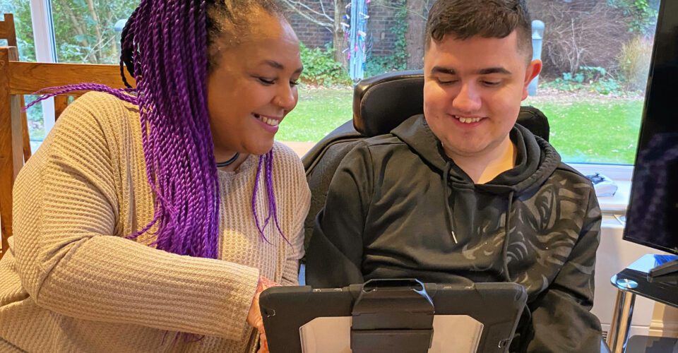 Woman and young person in a wheelchair looking at a computer tablet and smiling