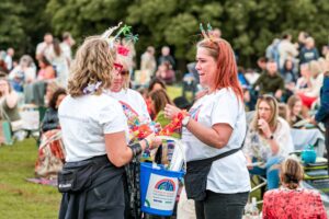 Three women wearing white t-shirts holding blue charity collection buckets and wearing party headwear