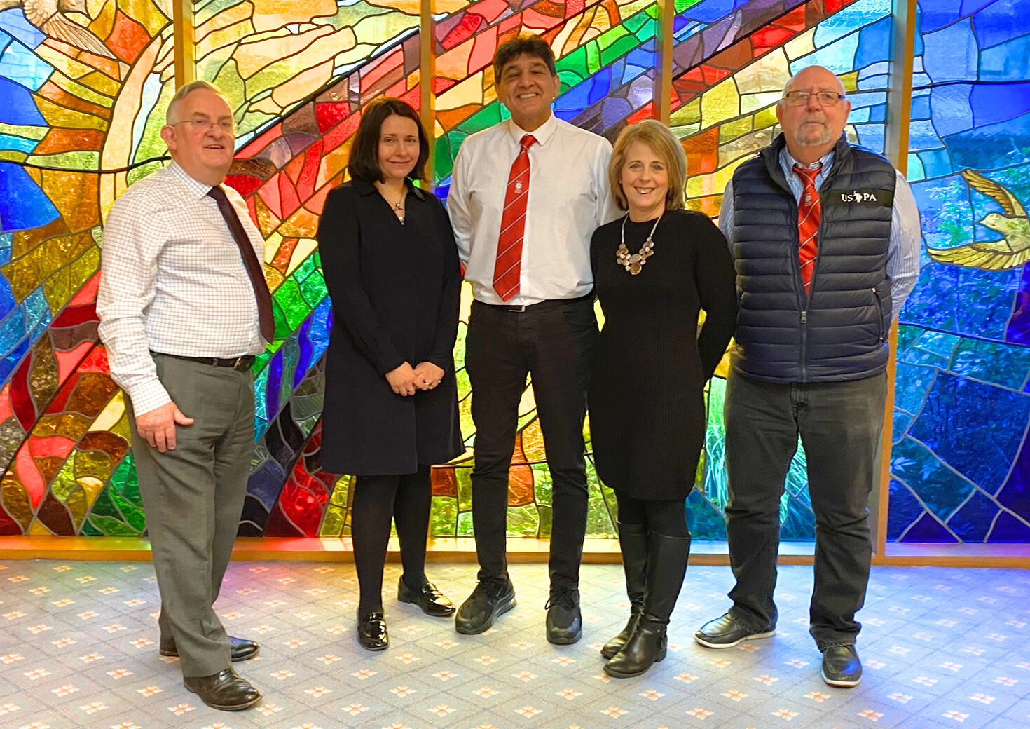 Three men and two women stood infront of a stained glass window