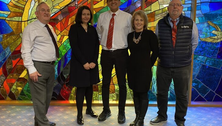 Three men and two women stood infront of a stained glass window