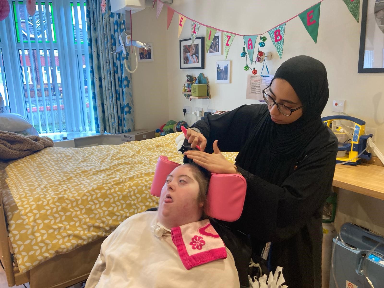 Woman brushing the hair of a young woman in a wheelchair in a bedroom setting with bunting