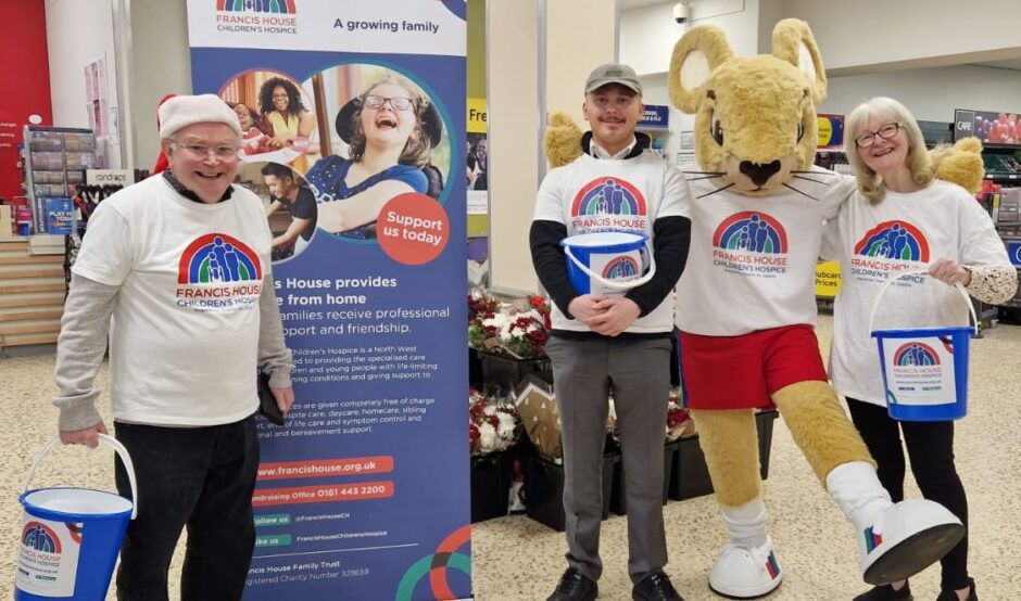 Three people wearing Francis House t-shirts stood holding buckets in a supermarket next to a large mouse mascot