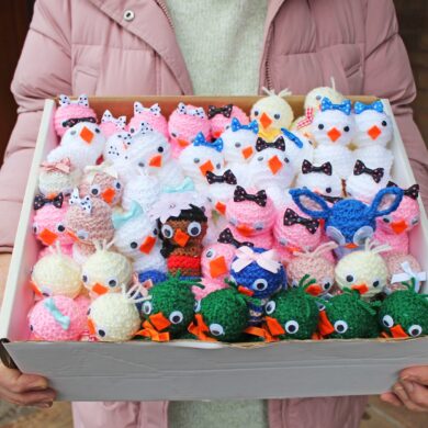 Box of knitted chicks being held by a woman wearing a pink coat