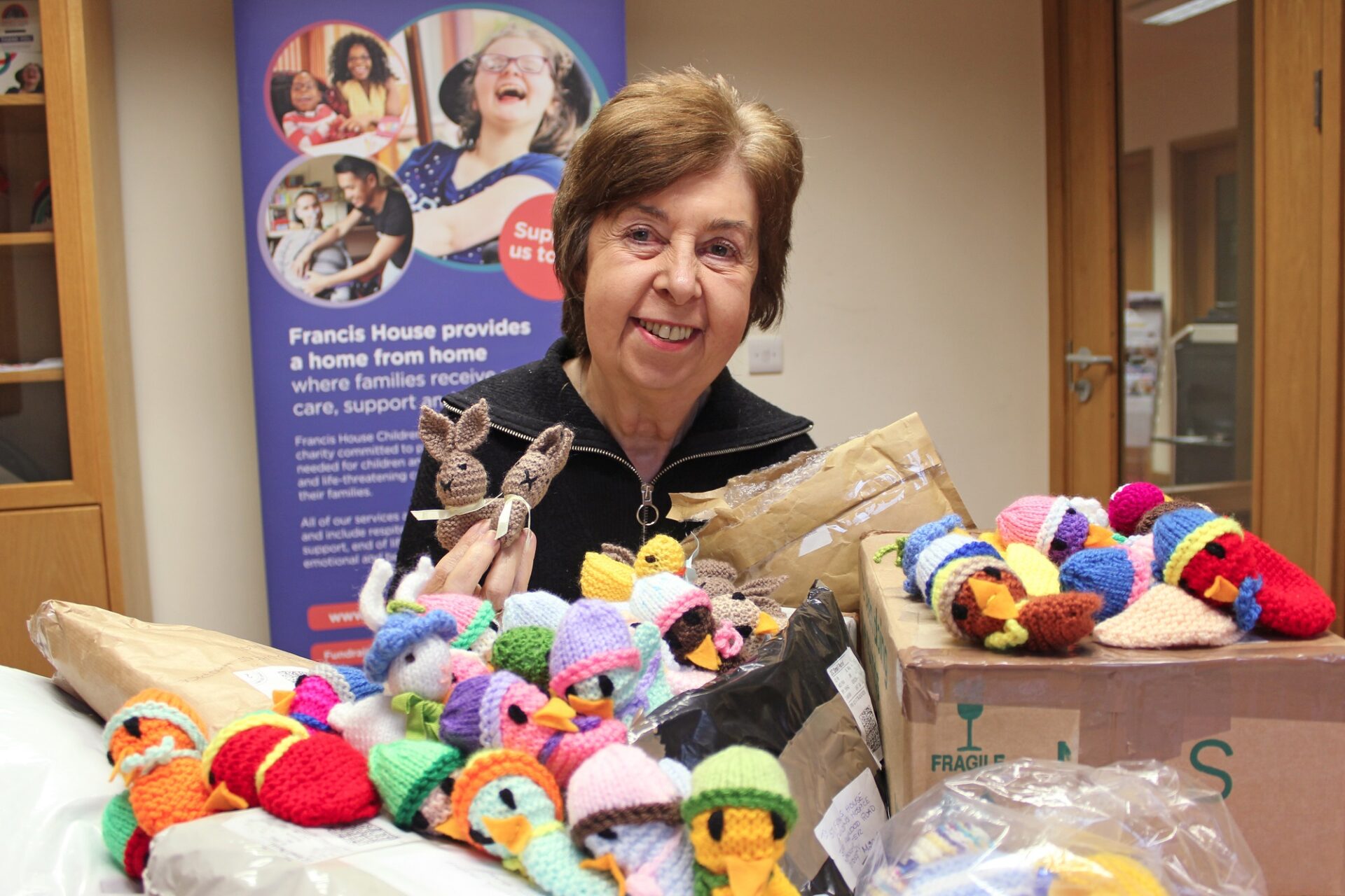 Woman holding knitted bunnies sat in front of parcels of knitted chicks