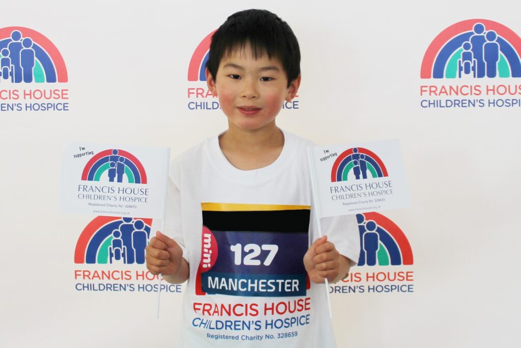 Boy wearing a running t-shirt and holding two flags stood in front of a banner