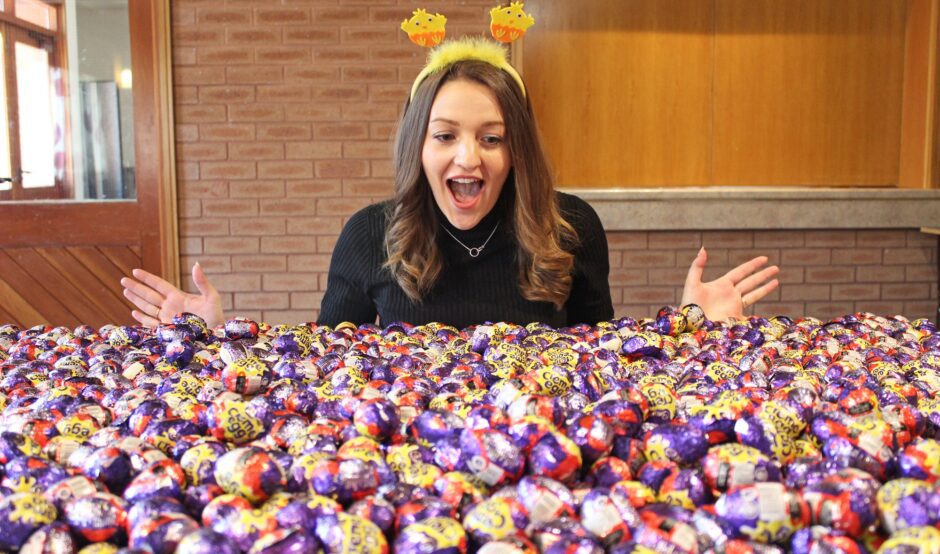 Woman looking a large pile of creme eggs with her mouth open and hands raised in a gesture of surprise