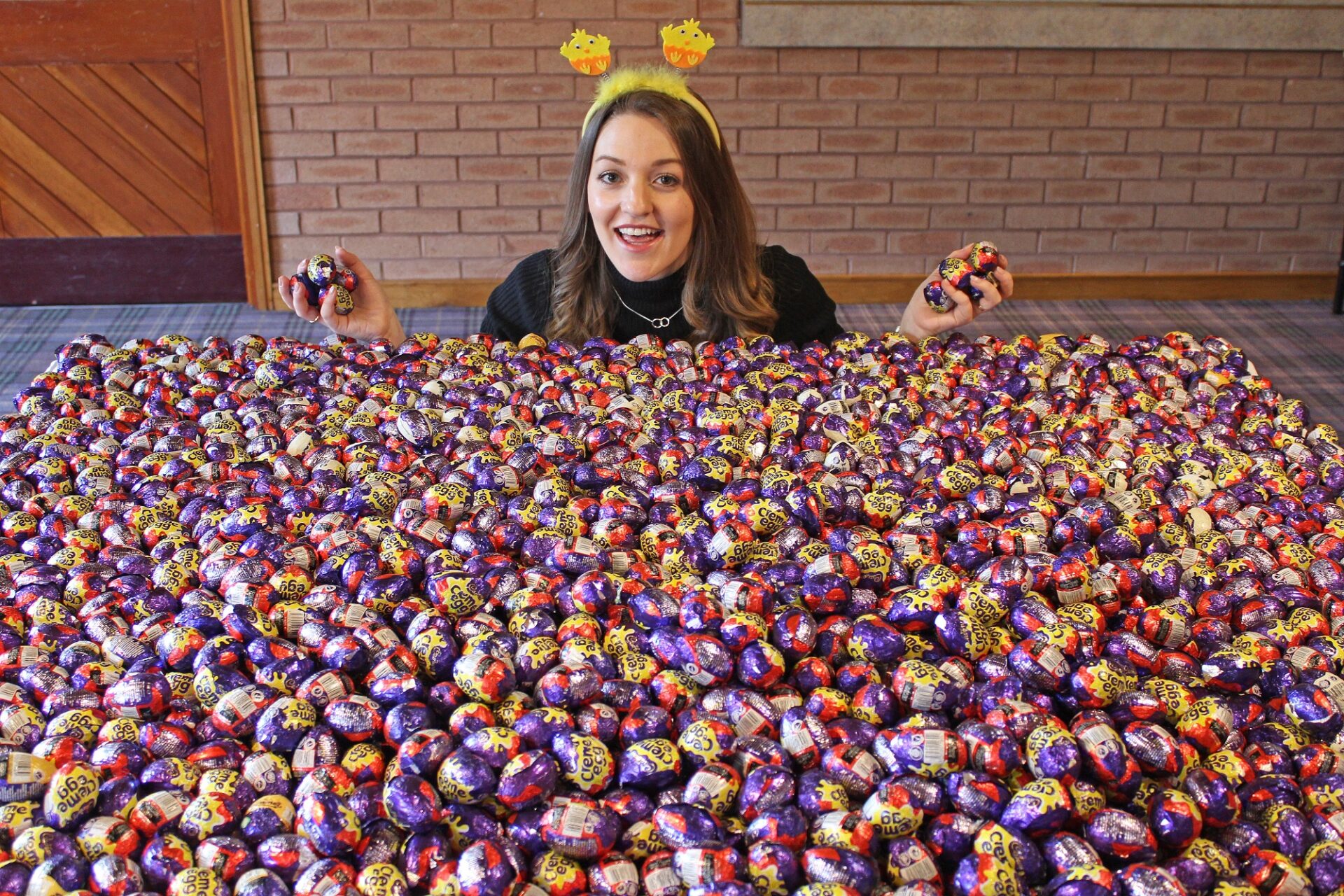 Woman holding chocolate creme eggs kneeling in front of thousands of creme eggs