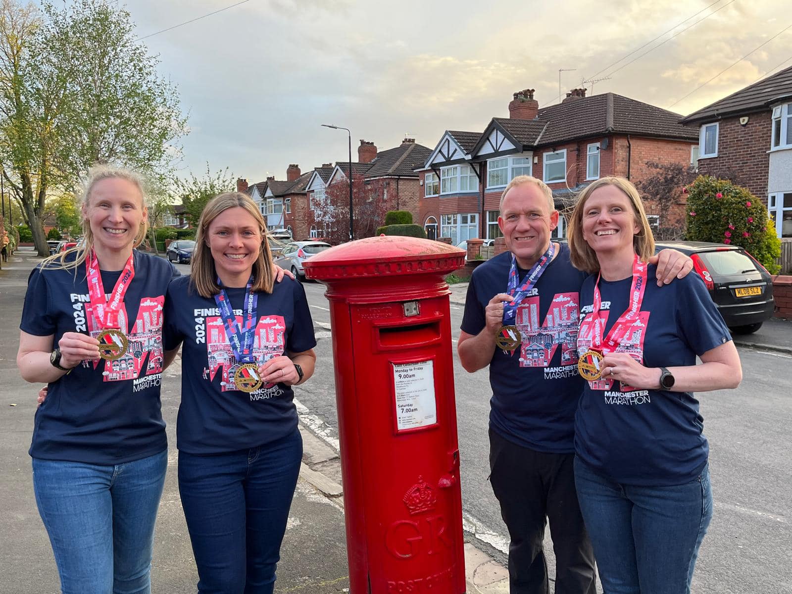 Four people holding running medals stood by a post box