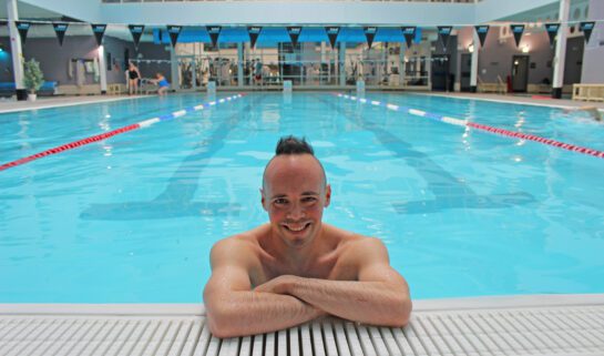 Man in a bright blue swimming pool resting his arms on the pool edge