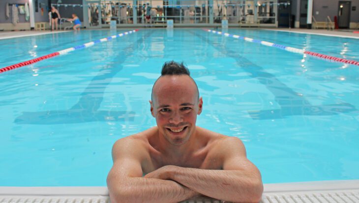 Man in a bright blue swimming pool resting his arms on the pool edge