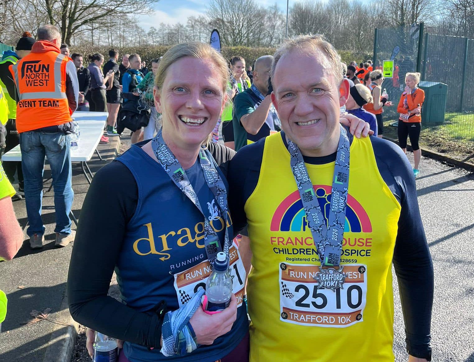 Woman and man wearing running vests holding medals