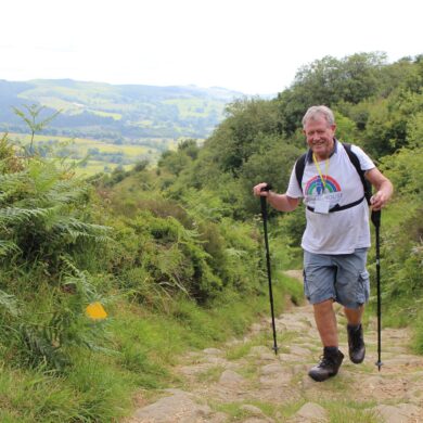 Hiker wearing white t-shirt and using walking sticks walks countryside path