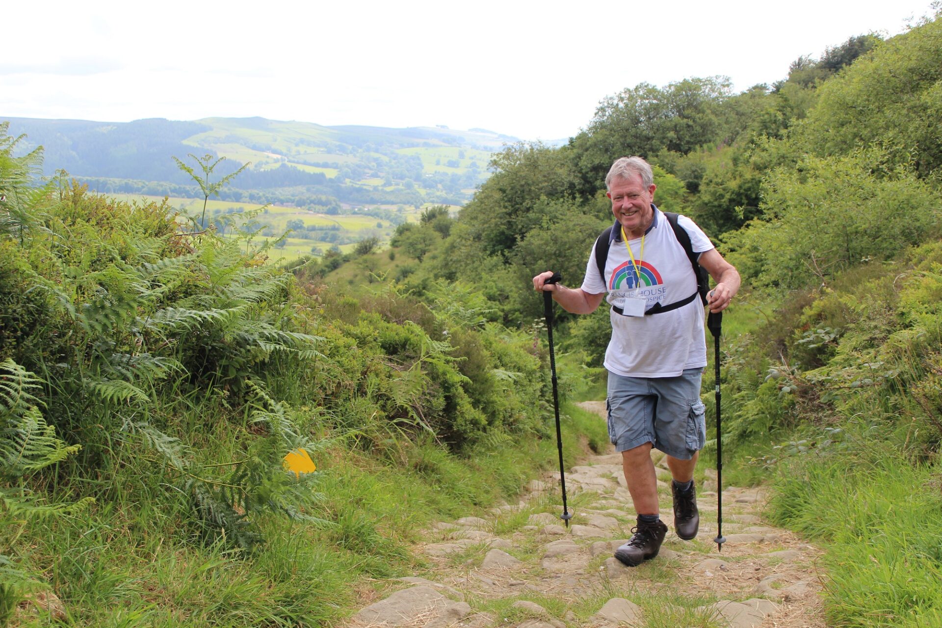 Hiker wearing white t-shirt and using walking sticks walks countryside path