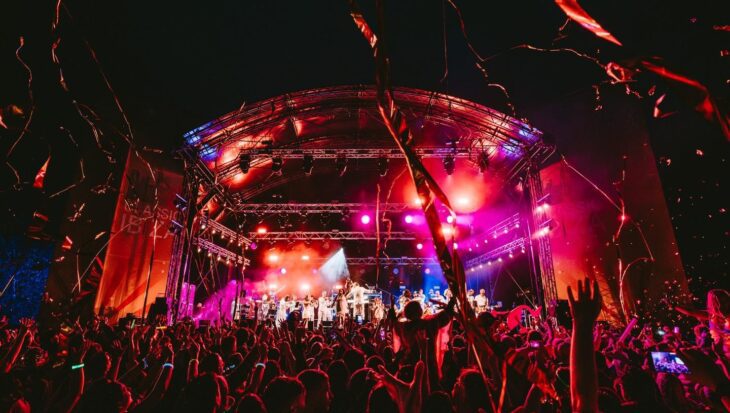 Crowds at a night time concert with stage lit by colourful lighting