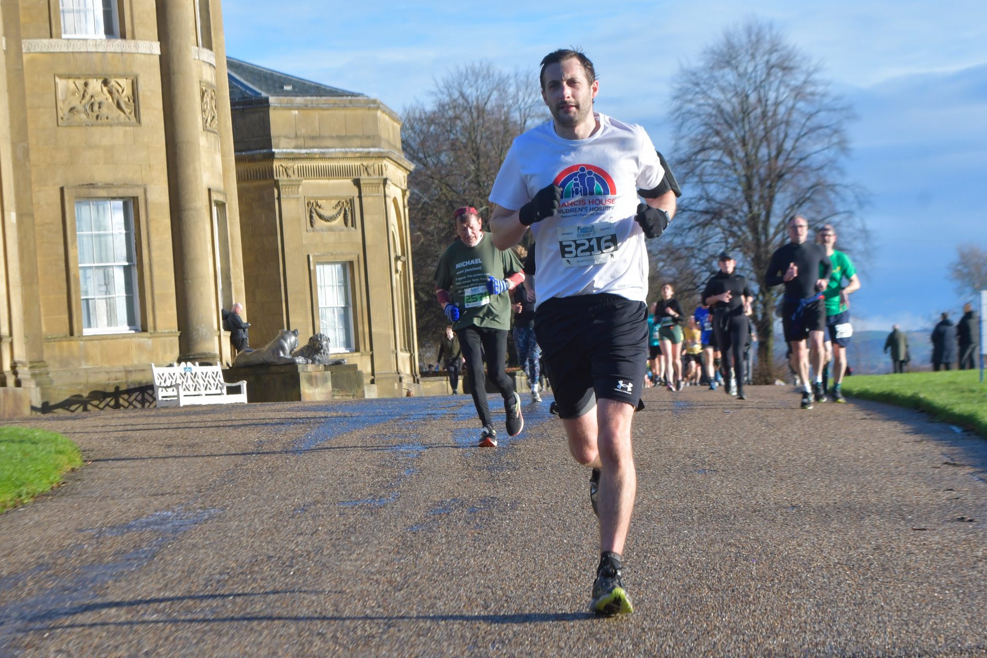 Man wearing a white t-shirt running on a path in front of a large country house