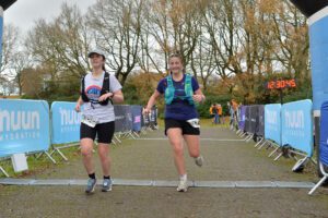Two female runners smiling crossing the finish line