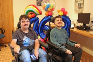 Two young men in wheelchairs in front of a balloon display