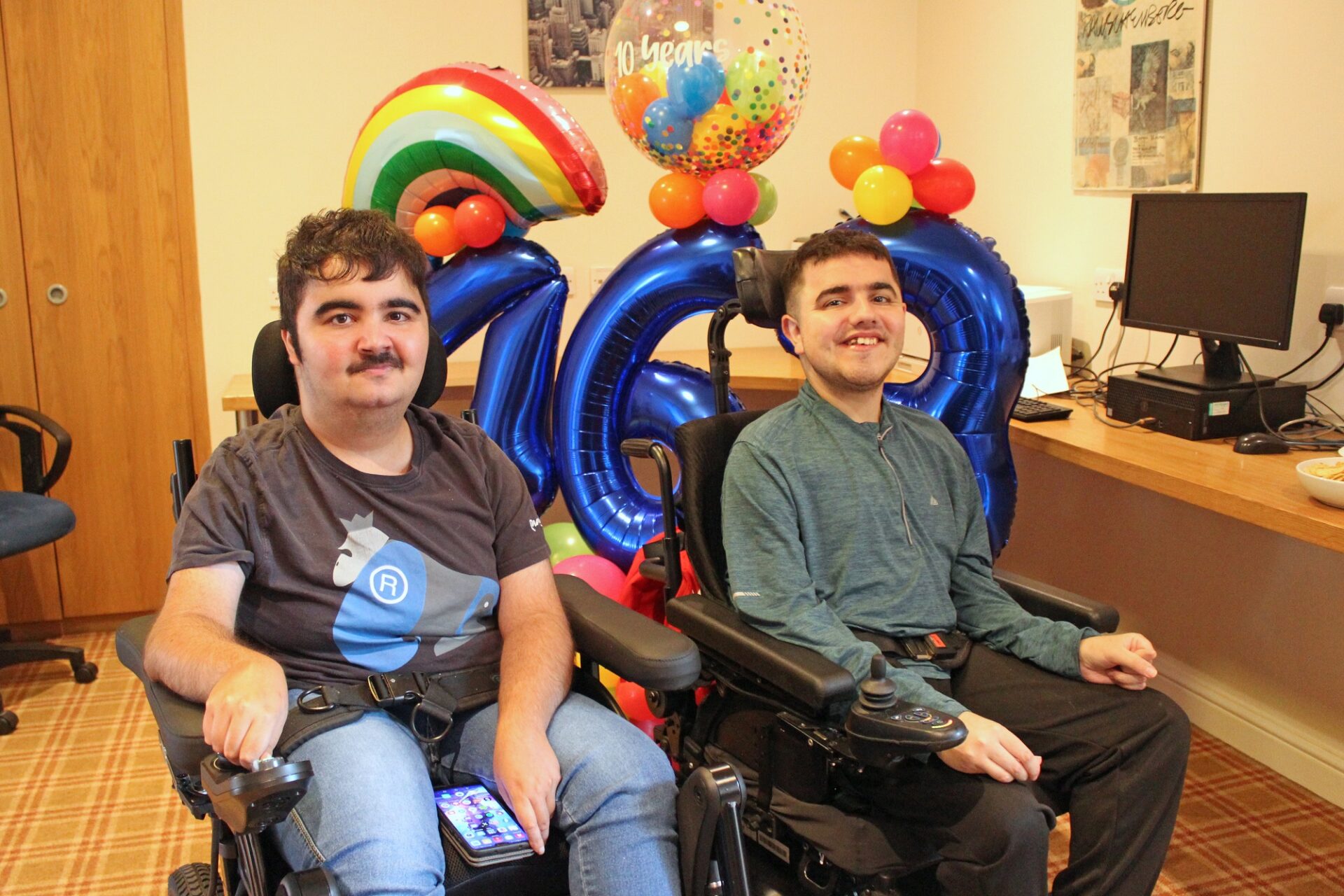 Two young men in wheelchairs in front of a balloon display