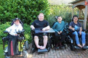 Four young adults in wheelchairs sat on a patio in a garden