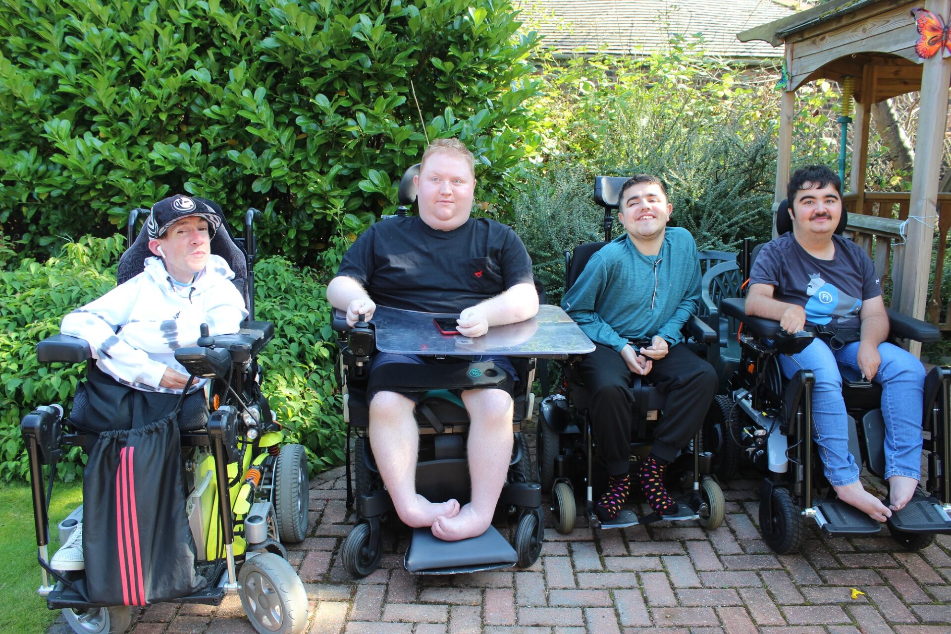 Four young adults in wheelchairs sat on a patio in a garden
