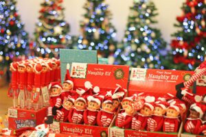 Naughty elf toys in a shop in front of a row of Christmas trees
