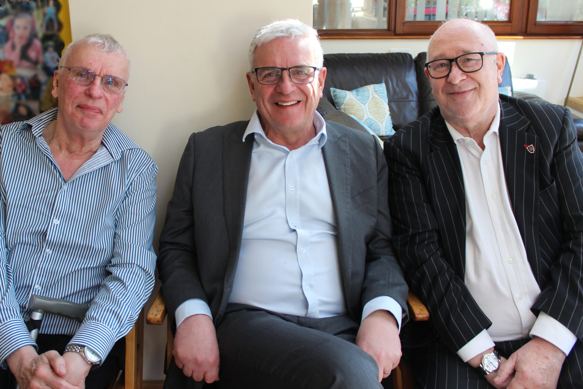 Three men seated wearing shirts and jackets smiling at the camera