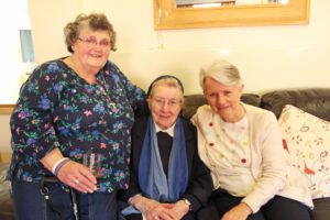 Three women sat on a sofa smiling at the camera