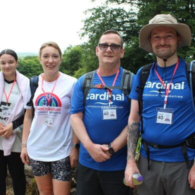 Two women and two men dressed in white and blue t-shirts stood against a stone wall in the countryside