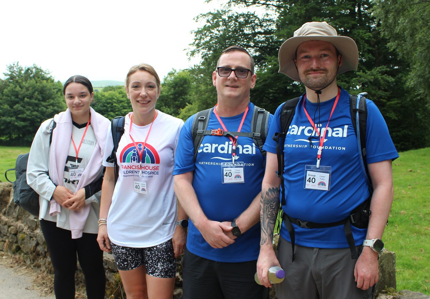 Two women and two men dressed in white and blue t-shirts stood against a stone wall in the countryside