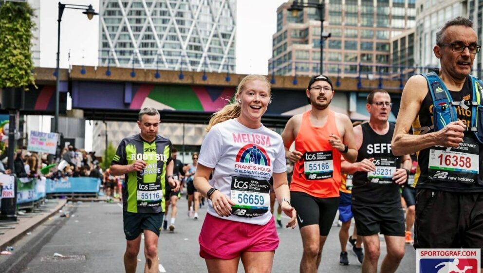 Men and women wearing running vests and shorts running the streets of London in the London marathon