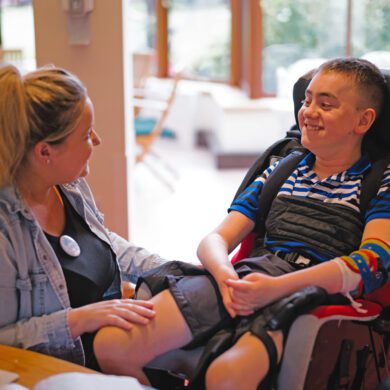 Woman sat with her hand on the knee of a boy in a wheelchair smiling at each other