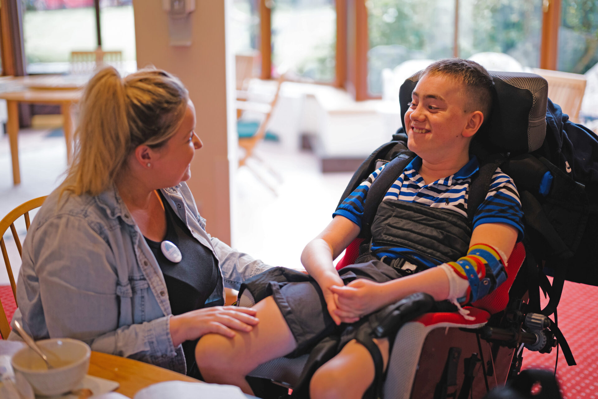 Woman sat with her hand on the knee of a boy in a wheelchair smiling at each other