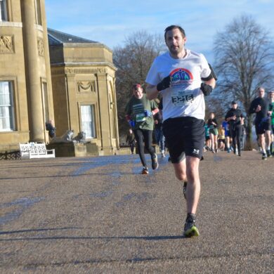 Man wearing running clothes running on a tarmac path outside of a large country house