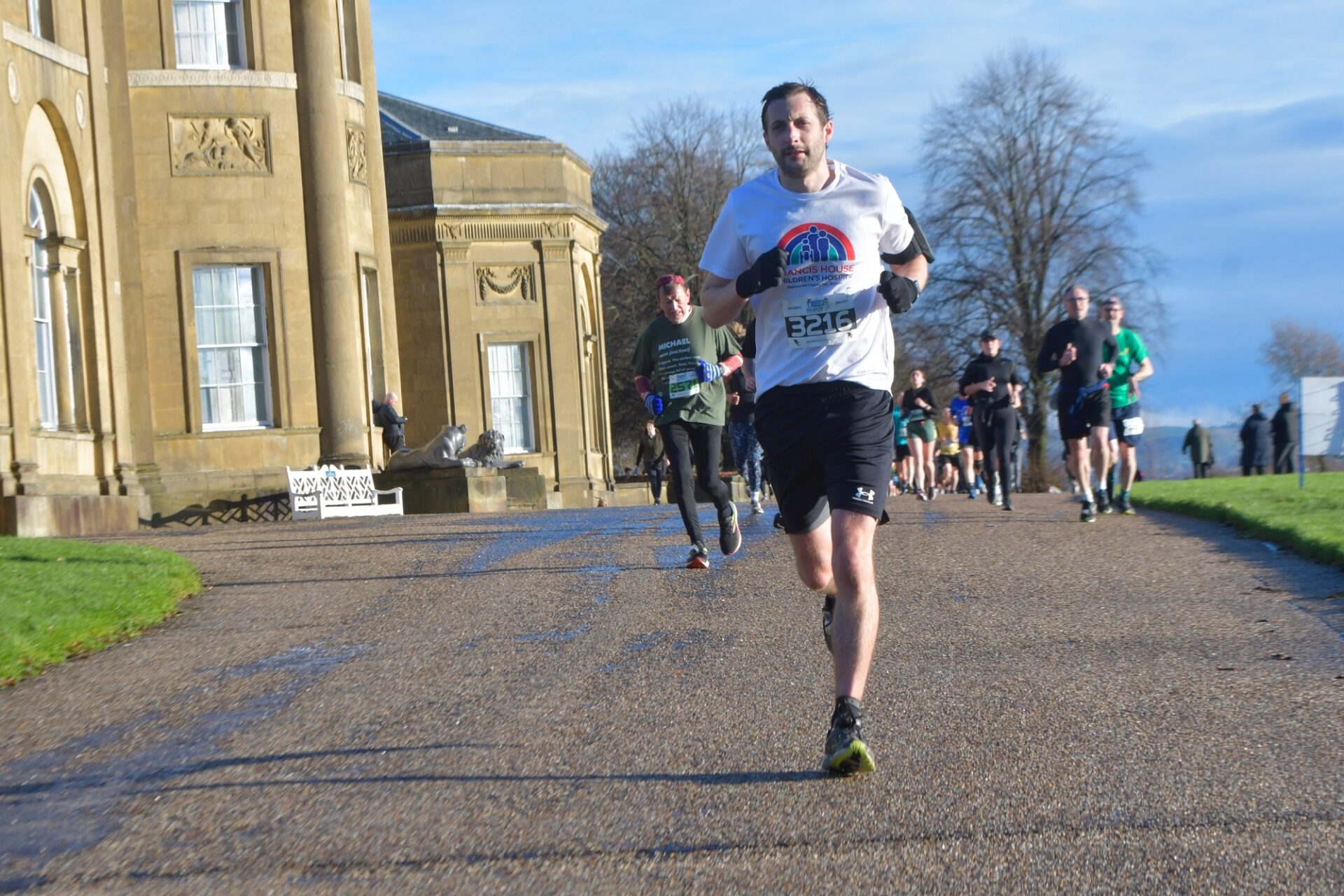 Man wearing running clothes running on a tarmac path outside of a large country house