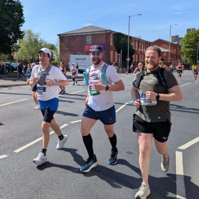 Three men running on the road with other runners around them smiling at the camera