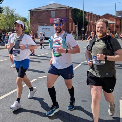 Three men running on the road with other runners around them smiling at the camera