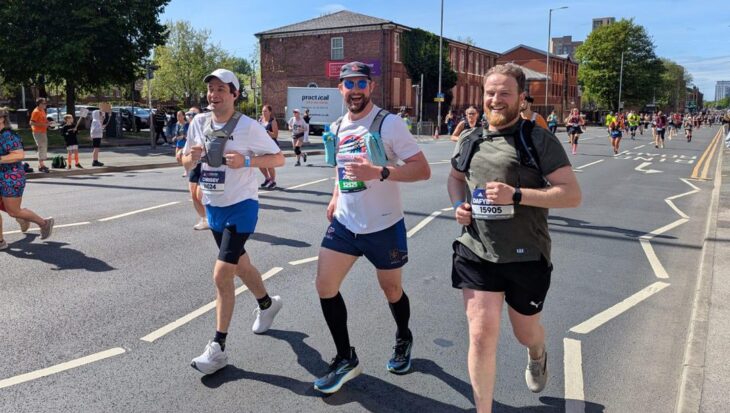 Three men running on the road with other runners around them smiling at the camera