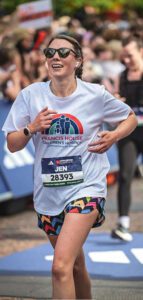 Woman wearing a white running t-shirt running with crowds in the background during the London Marathon