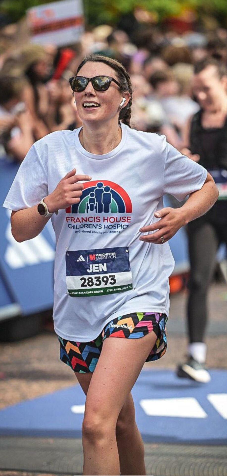 Woman wearing a white running t-shirt running with crowds in the background during the London Marathon