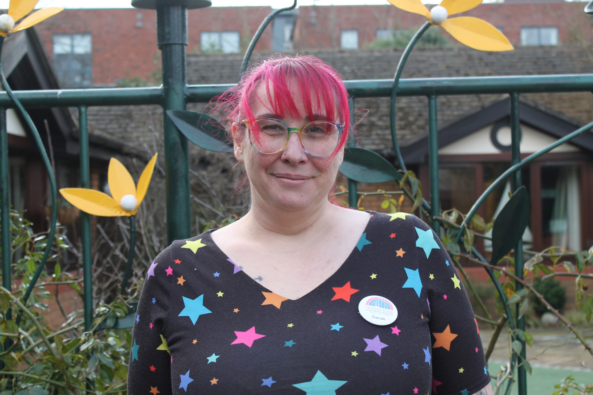Woman with red hair wearing a top with coloured stars smiling at the camera
