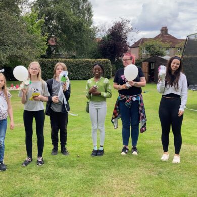 Group of young people stood on a grassy lawn holding balloons