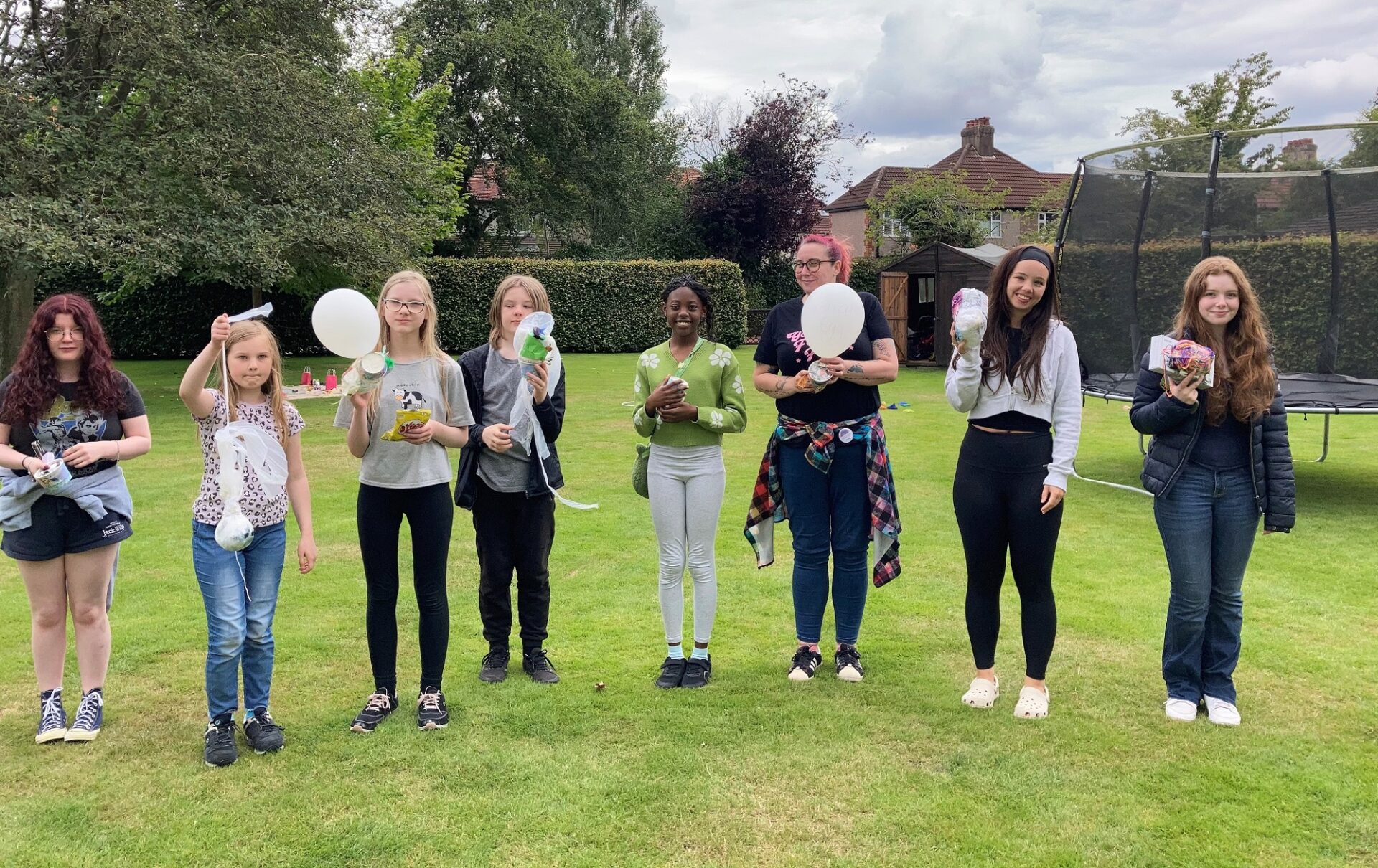 Group of young people stood on a grassy lawn holding balloons