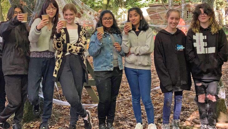 Group of young people stood in a forest holding paper coffee cups and smiling at the camera