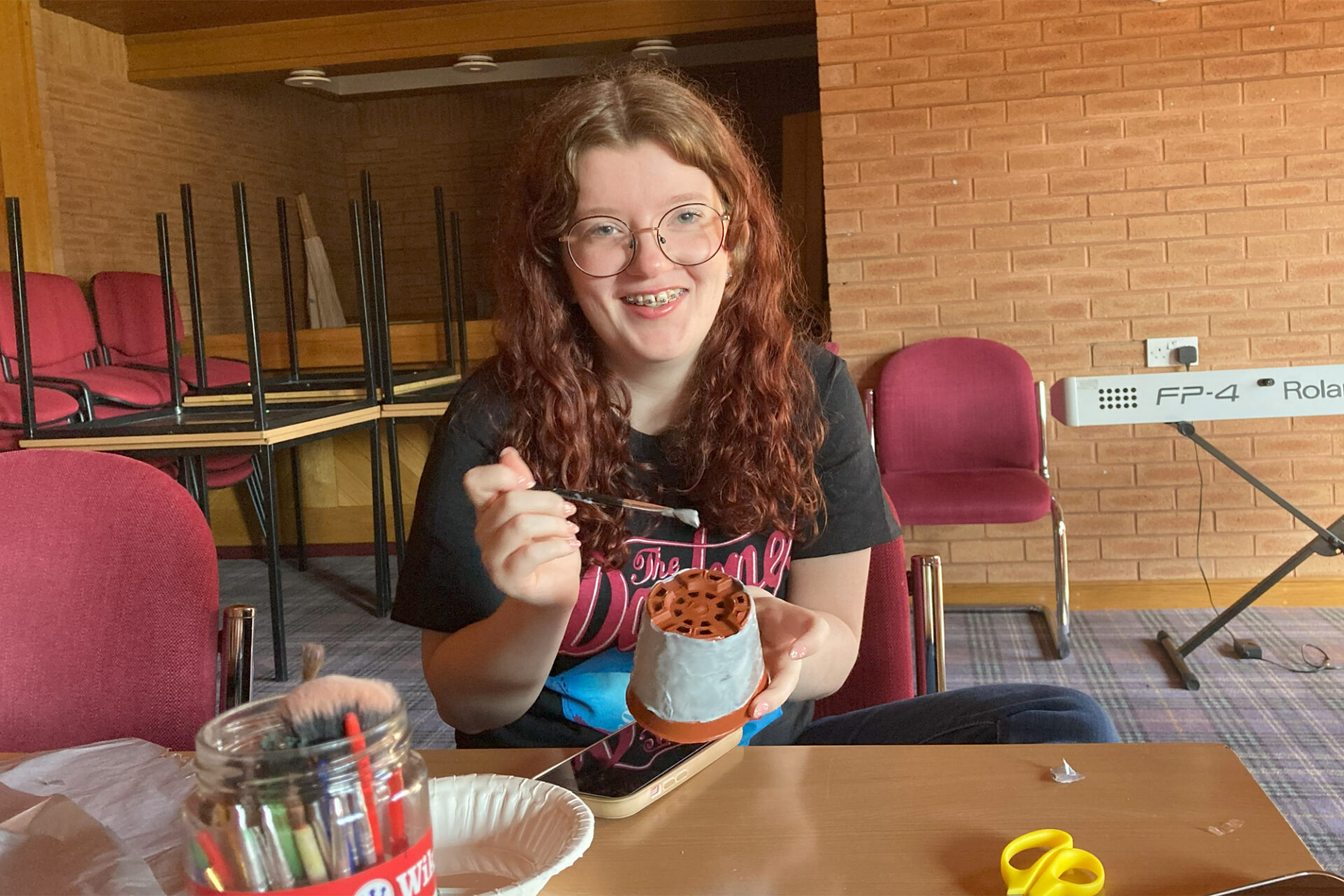 Young girl painting a flower pot smiling at the camera
