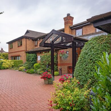 Francis House a brick building with a brown wooden entrance and shrubs and bushes planted on a brick drive way.
