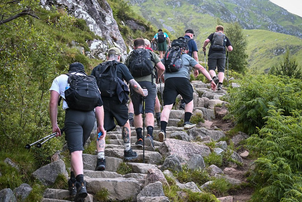 Group of men wearing hiking gear walking up steep stone steps surrounded by bushes and hills away from the camera